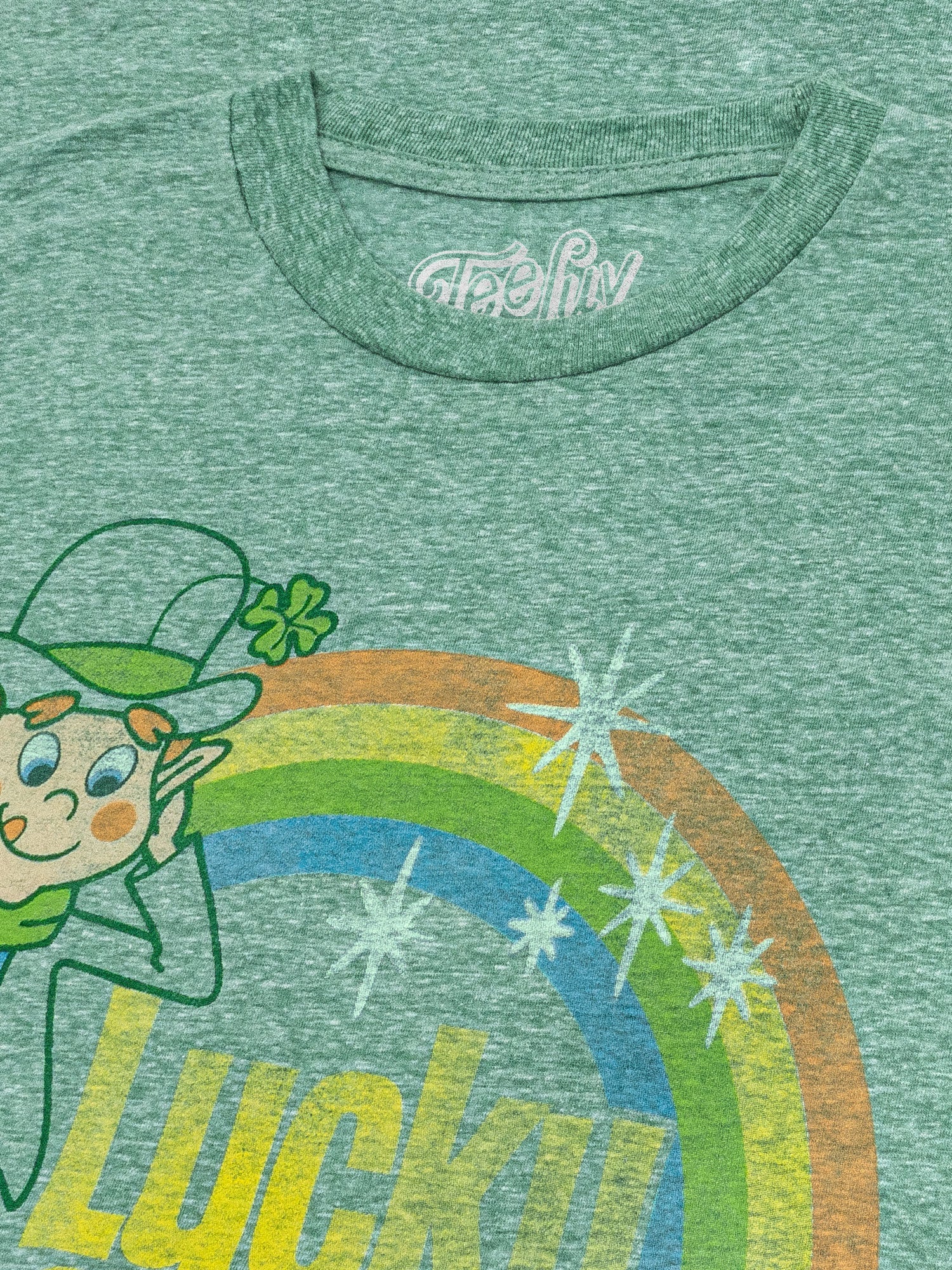 Green t-shirt with a cartoon leprechaun and rainbow design, featuring the brand 'Artful'.