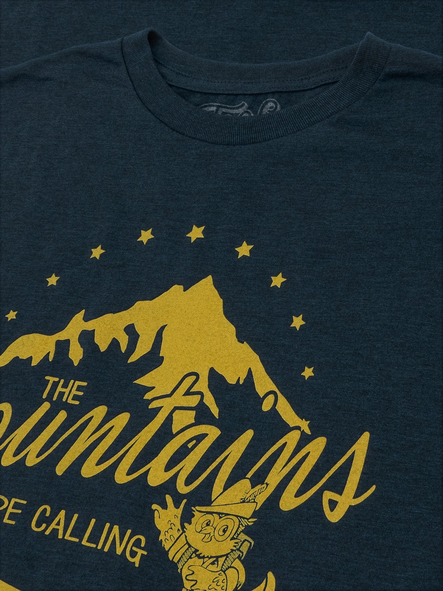 Navy blue t-shirt with yellow mountain graphic and text 'The Mountains Are Calling' on a dark background