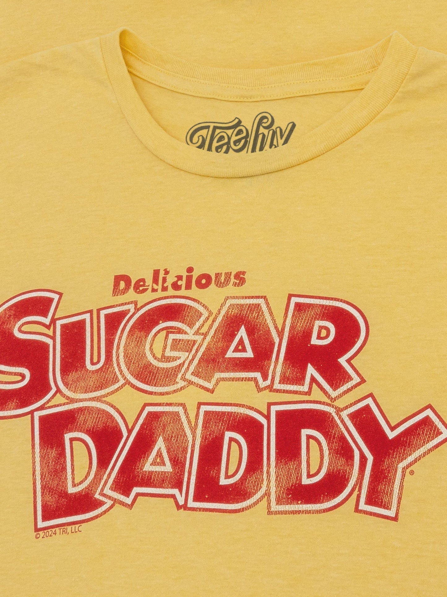 Yellow t-shirt with red and white text 'Delicious Sugar Daddy' on a yellow background